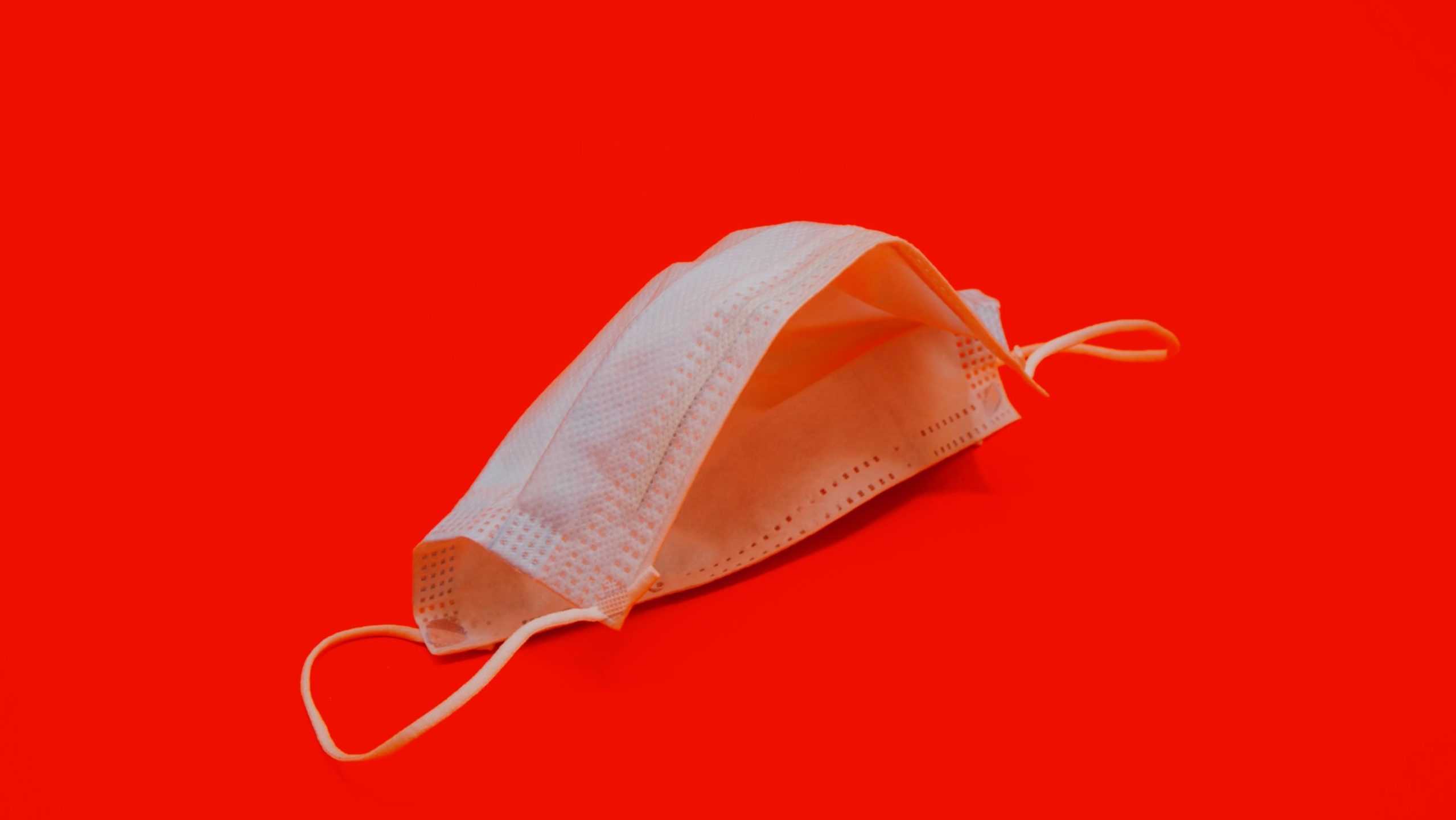 máscara descartável branca sobre fundo vermelho; máscaras inibem a transmissão por aerossóis