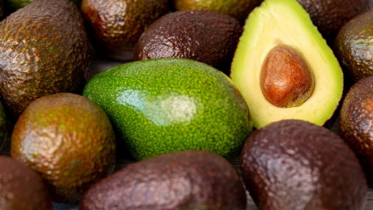 Abacates maduros agrupados, com um abacate cortado ao meio exibindo a polpa verde e o caroço.