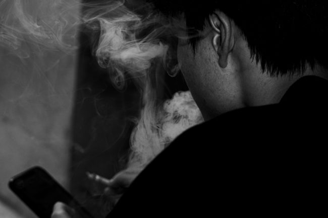 Jovem usando cigarro eletrônico, envolto em fumaça, ilustra preocupação crescente com a saúde vocal e respiratória entre brasileiros.