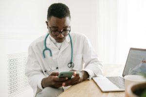 Profissional de saúde usa celular e computador em consultório.