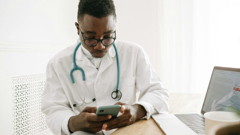 Profissional de saúde usa celular e computador em consultório.