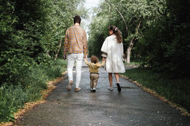 pexels-shvetsa-4586686 Pais caminhando de mãos dadas com filho pequeno em parque.