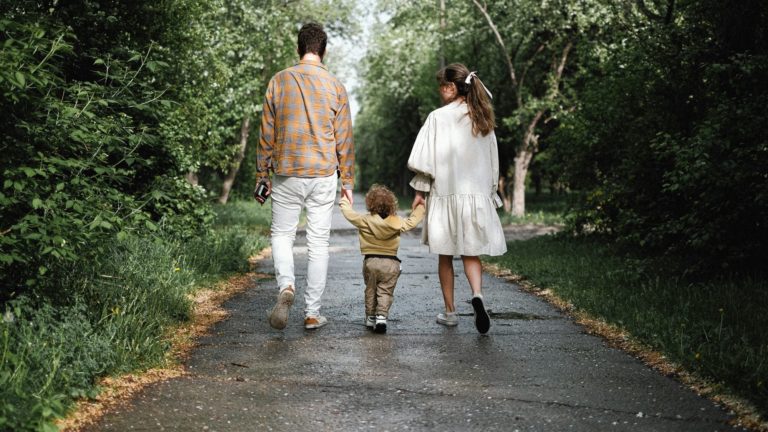 pexels-shvetsa-4586686 Pais caminhando de mãos dadas com filho pequeno em parque.