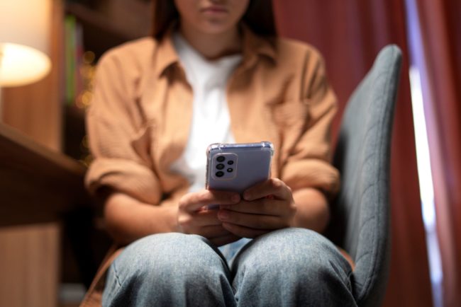Adolescente olha para o celular, representando sofrimento psíquico e automutilação em tempos de pandemia