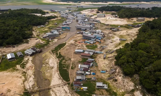 Comunidade ribeirinha na Amazônia com barcos encalhados e rio seco durante forte estiagem, evidenciando os efeitos das mudanças climáticas.