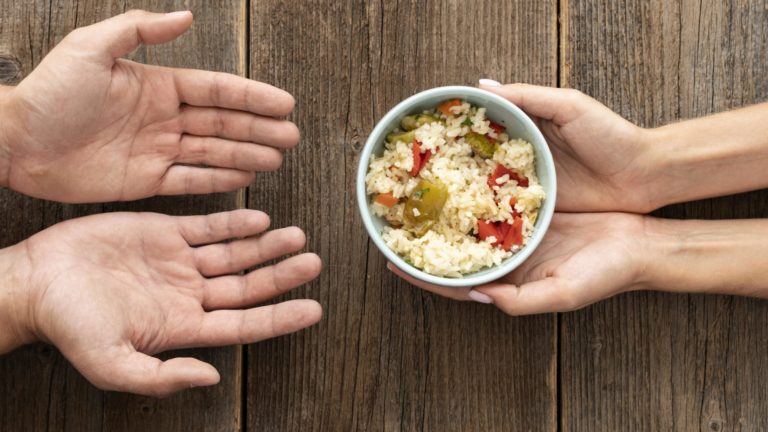 Mãos estendidas recebem um prato simples de comida, simbolizando o impacto da alta dos preços e a desigualdade no acesso à alimentação.