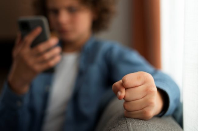 Adolescente segura o celular com expressão de tensão, simbolizando o impacto emocional da violência online e do cyberbullying