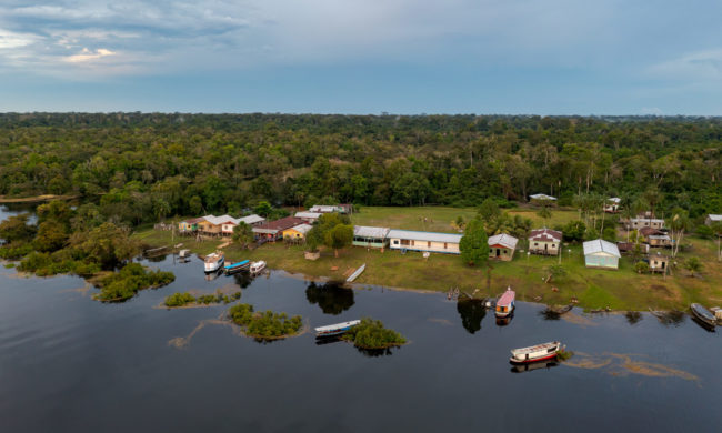 amanã Casas ribeirinhas de madeira à beira d’água na Reserva Amanã, no Amazonas, cercadas por vegetação e pequenas embarcações, retratando o cotidiano das comunidades que lidam com o acúmulo de resíduos plásticos.