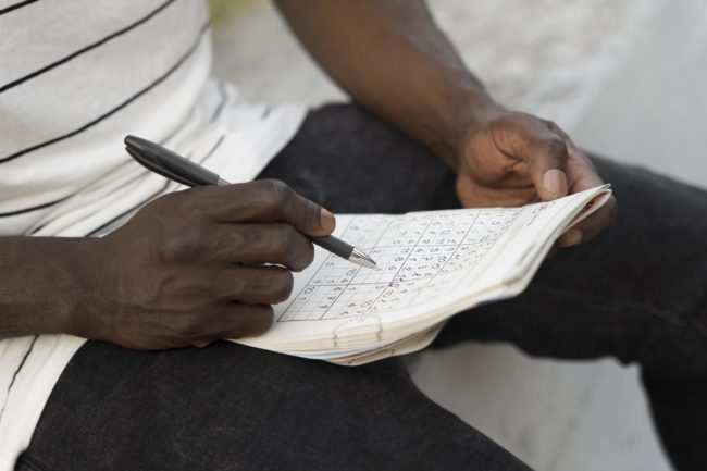 Pessoa segurando um caderno de sudoku e marcando números com caneta