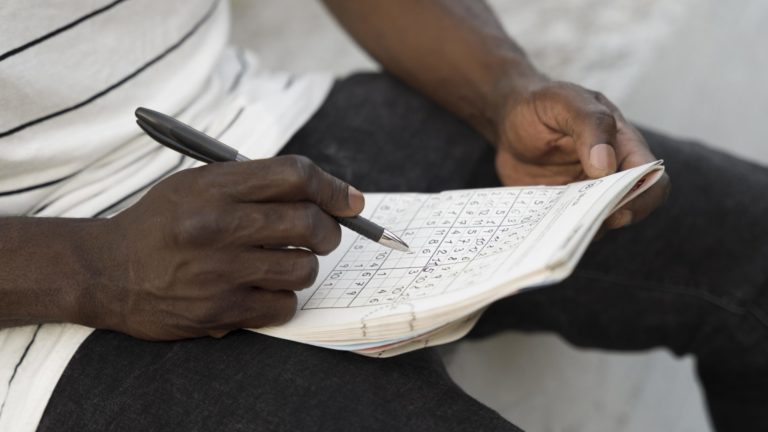 Pessoa segurando um caderno de sudoku e marcando números com caneta