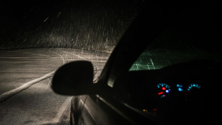 Carro dirigindo à noite sob chuva, com estrada molhada à frente