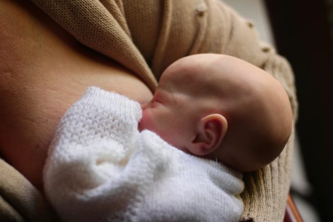 Bebê recém-nascido amamentando no colo da mãe, visto de perfil, com foco na sucção e no contato boca-seio